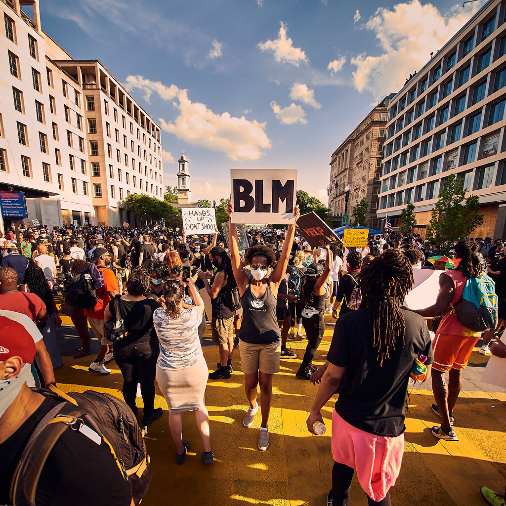 A masked member of a crowd holds up a BLM sign