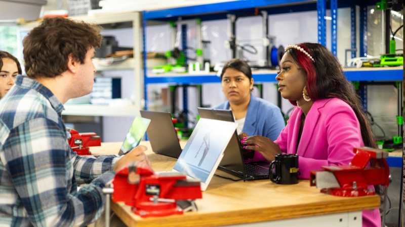 A group of people sitting at a table with laptops.