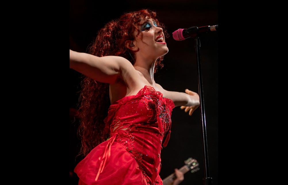 The singer Chapell Roan in a red silk dress, gesturing exuberantly at the Hollywood Palladium in 2022.