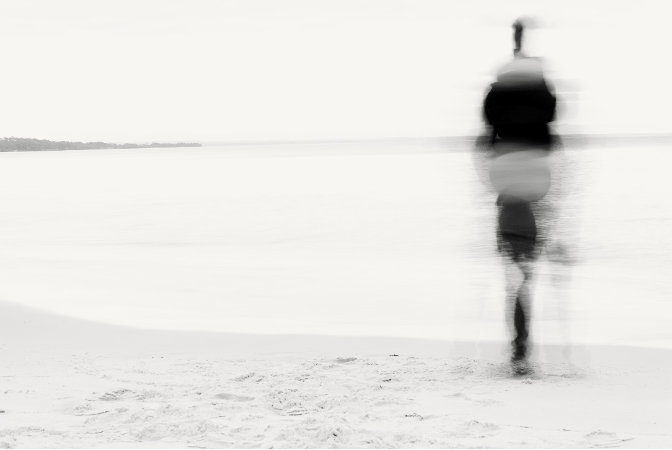 image of a beach in black and white, with a blurry person walking
