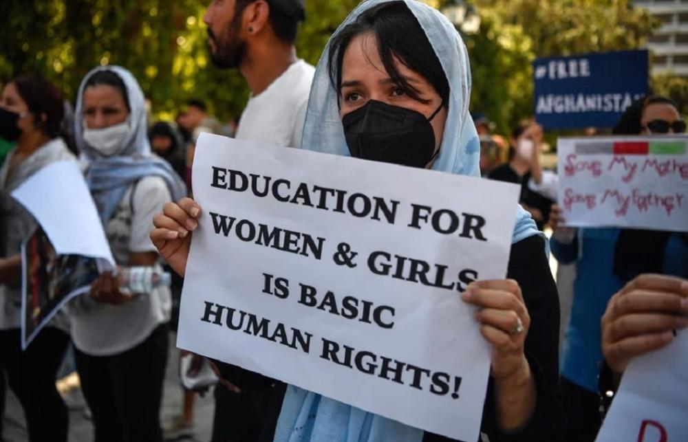 woman at a protest, holding a sign saying 'education for women and girls is basic human rights!'