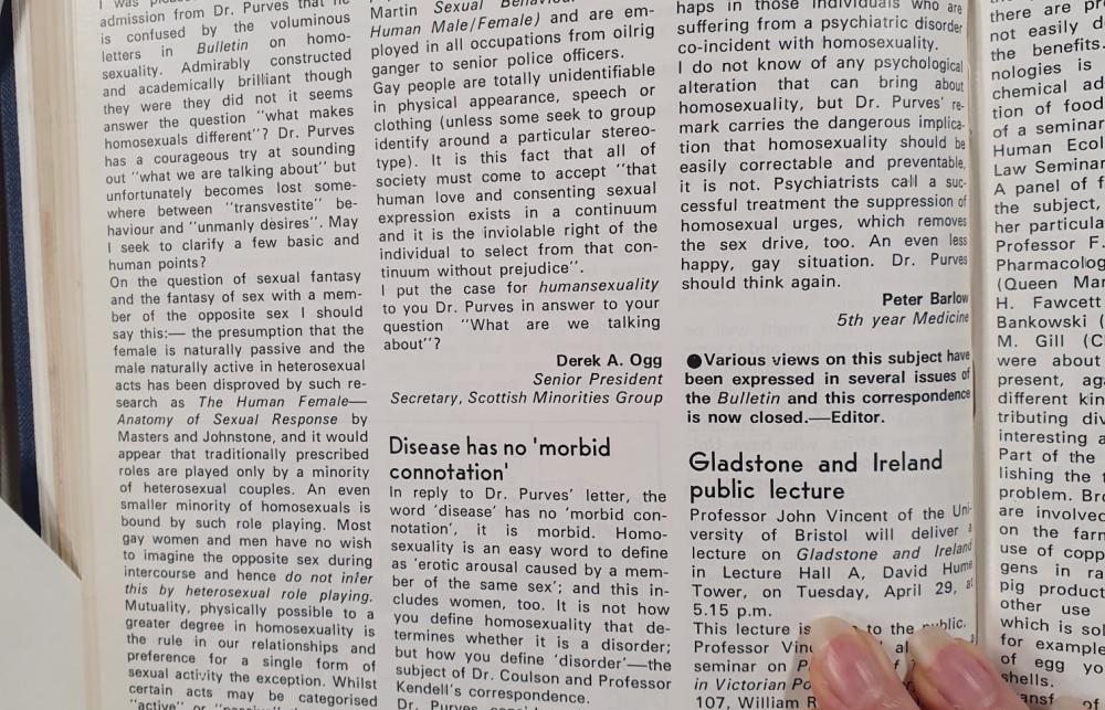 A hand holding down an archival newspaper