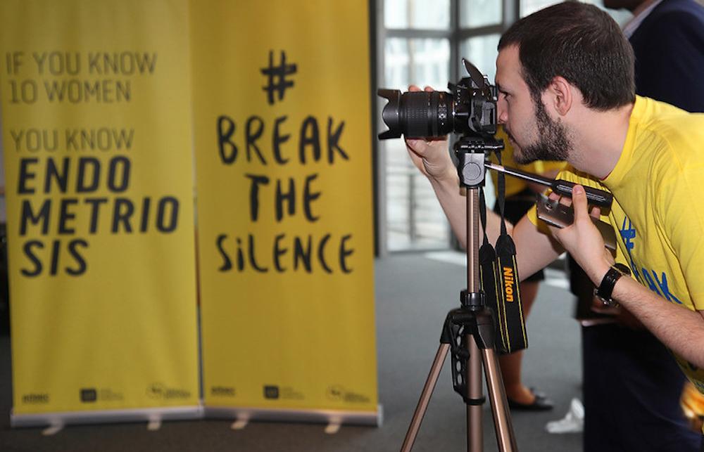 Person in a yellow T-shirt photographing an Endometriosis Awareness signboard