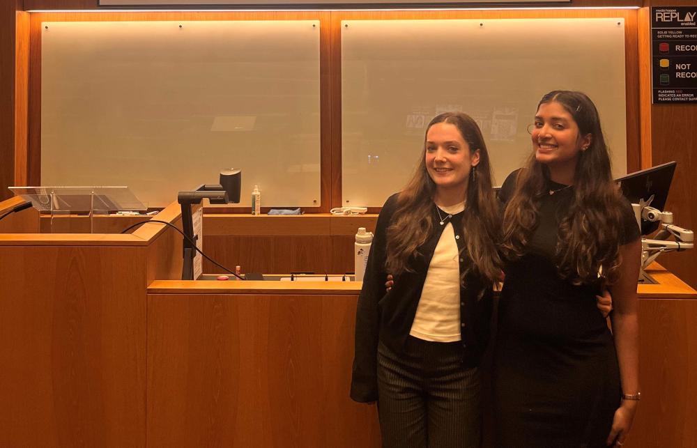 Photo of Thulsa Miqdhaadh Moosa and a friend standing at the front of a lecture hall. Behind them is a screen that reads 'Afghan Women Leading Panel Change: Panel Event' 
