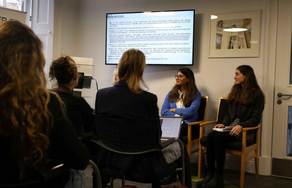 Photo of Sarah, Elif, and Patricia Jefferey at the International Women's Day event during the panel discussion. They are sitting in a row under a screen that reads 'references'. There are sitting in front of a group of an audience. 