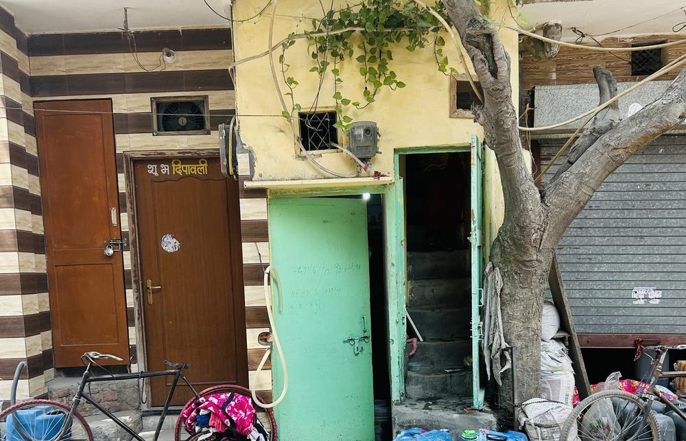 An image of two houses taken during fieldwork in Delhi, with trees, bicycles and containers outside the homes.